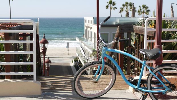 Blue bicycle, cruiser bike by ocean beach, pacific coast, Oceanside California USA. Summertime vacations on sea shore. Vintage cycle near wooden stairs, stairway access. Staircase, tropical palm trees