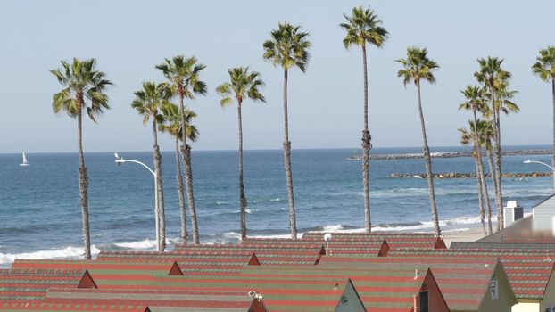 Colorful waterfront cottages in Oceanside, California USA. Multicolor bungalow huts by sea, beachfront lodging. Many vacation houses on beach, ocean waves and palm trees. Summer seascape on sunny day.