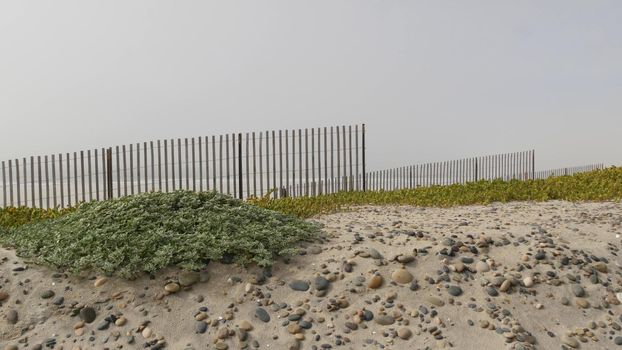 Wooden picket fence, sandy misty beach, Encinitas California USA. Pacific ocean coast, dense fog on empty sea shore. Coastline near Los Angeles, boards in milky smog haze. Gloomy weather on shoreline.