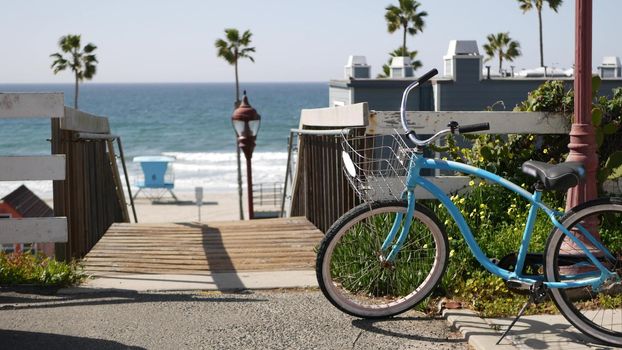 Blue bicycle, cruiser bike by ocean beach, pacific coast, Oceanside California USA. Summertime vacations sea shore. Vintage cycle by wooden stairs, stairway or staircase. Tropical palms and lifeguard