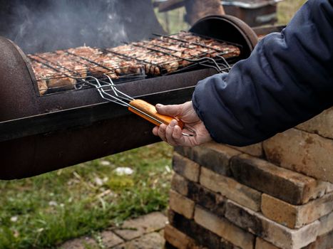 Woman turns meat over for barbecue on grill.