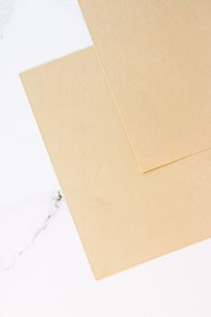 Beige A4 papers on white marble background as office stationery flatlay, luxury branding flat lay and brand identity design for mockups