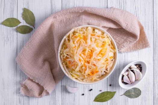 Top view of a ceramic bowl with fermented sauerkraut and spices on a light wooden surface. Healthy food concept. Selective focus.