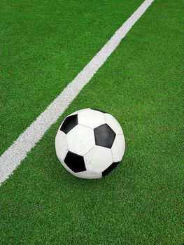 Close up one black and white football ball over green artificial turf of soccer field pitch with white marking lines, elevated, high angle view, personal perspective