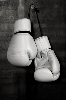 Close up pair of white leather boxing gloves hanging over black wall with copy space