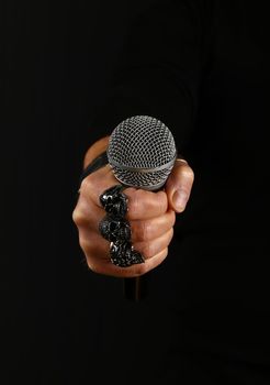 Close up man hand with metal rings and bracelet holding microphone over black background, side view