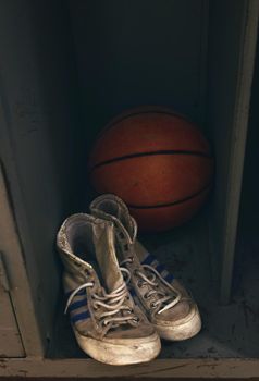 Close up pair of old worn sport sneakers shoes and one basketball ball in locker, high angle view