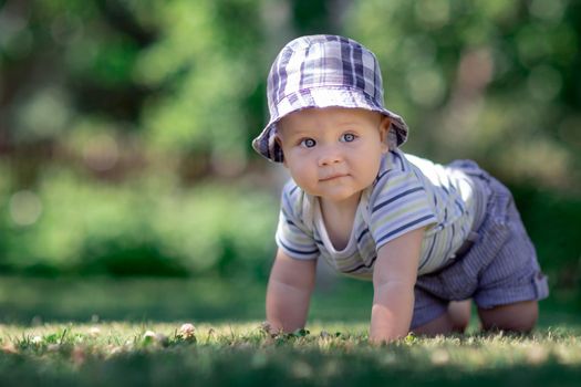 Baby with nice blue cap crawling on the green grass in the garden and smiles