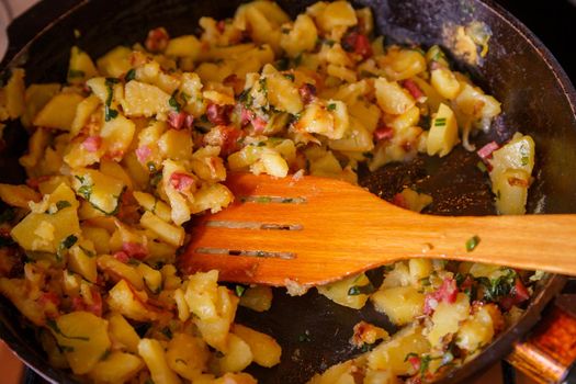 roasted domestic potatos in a frying pan with wooden spatula close-up with selective focus.