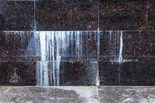 flat wall with rectangular natural tan brown granite tiles with white mineral drips.