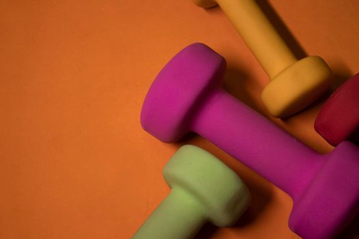 multicoloured small dumbbells on orange background. Sport concept