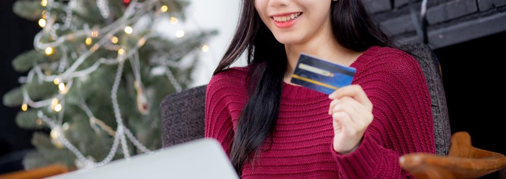 Young asian woman online shopping in Christmas with credit card on laptop computer, female buying and payment with debit card, xmas in holiday, happy new year, customer with purchase to internet.