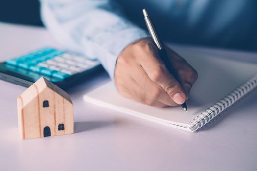 Hand of businessman planning and writing on note expense and mortgage with home, insurance house, finance and investment, calculate loan of residential, cost for refinance of property concept.