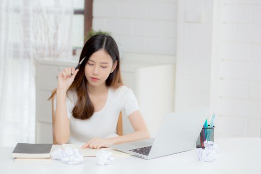 Young asian woman working with laptop computer think idea project and paper crumpled having problem on table at home, girl using notebook with frustrated and trouble, business and freelance concept.