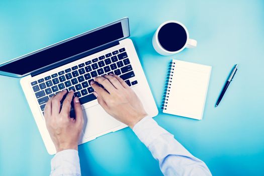 Flat lay, hand of businessman working on laptop computer with cup of coffee on desk in office, workplace and notebook and book on blue background, workspace and copy space, top view, business concept.