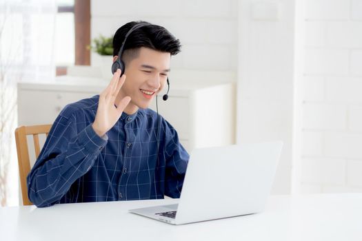 Young asian businessman working on laptop computer wearing headphone at home, business man wearing headset for video conference, communication and education, male study and learning for e-learning.