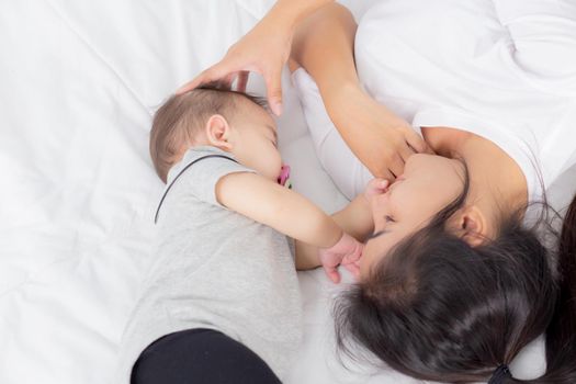 Young asian mother touch head of little baby girl with tender on bed in the bedroom, mom love newborn and care, woman with expression with child together, parent and daughter, family concept.