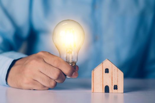 Businessman holding light bulb while home wooden for solution innovation and environment, thinking idea for planning buy house, residential with eco and saving energy, business and finance concept.