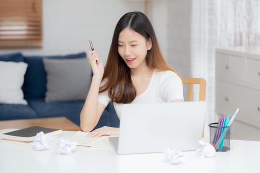 Young asian woman confident working at home with laptop computer and thinking idea for planning, freelance happy girl excited and success using notebook thoughtful and writing, business concept.