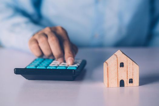 Hand of businessman planning and calculate expense and mortgage with calculator and home on desk, insurance and budget of residential, examining of loan and residence, business and property concept.