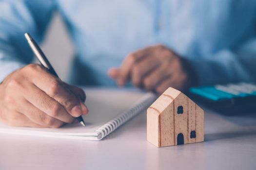 Hand of businessman planning and writing on note expense and mortgage with home, insurance house, finance and investment, calculate loan of residential, cost for refinance of property concept.