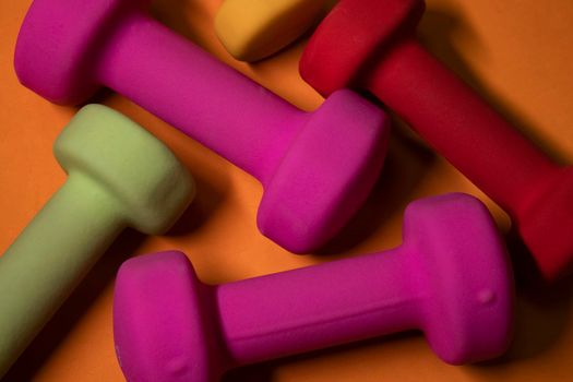 pink, green, red and yellow small dumbbells on orange background. Sport concept