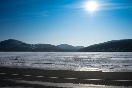 Seascape with bright sun and snow-covered shore.
