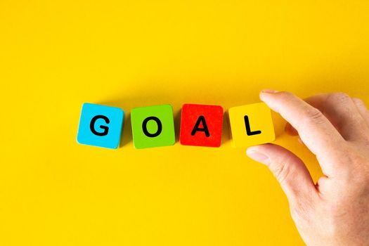 Man hand placing the wooden cubes with the word GOAL on yellow background. Business goal setting concept.