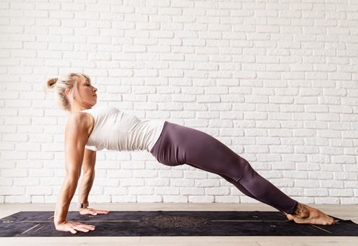 Active lifestyle. Young attractive woman wearing sportswear practicing yoga at home. Indoor full length, white brick wall background