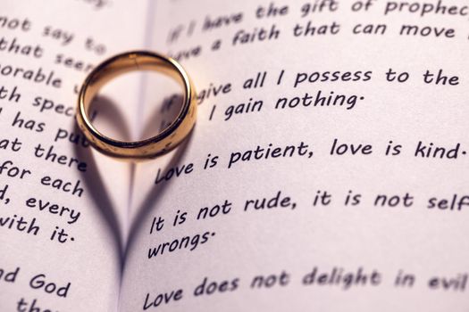 One golden wedding ring on Holy bible book with heart shaped shadow close up