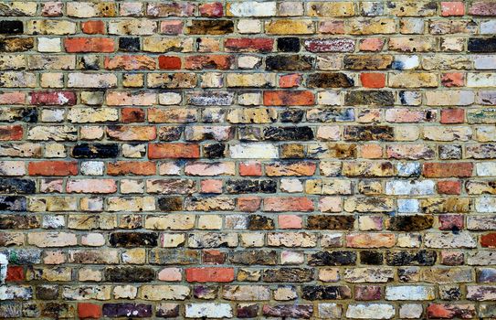 Photograph of a brick wall pattern. The bricks are pastel shades of yellow, red and pink.