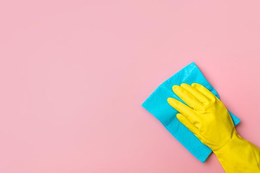 Employee hand in yellow rubber protective glove hold blue rag wiping pink wall background. House cleaning service, general or regular cleanup concept. Empty place for text or design