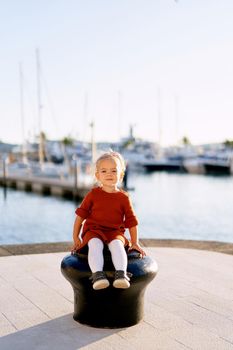A portrait of a pretty 2-year old girl sitting on a boat pier by the sea. High quality photo