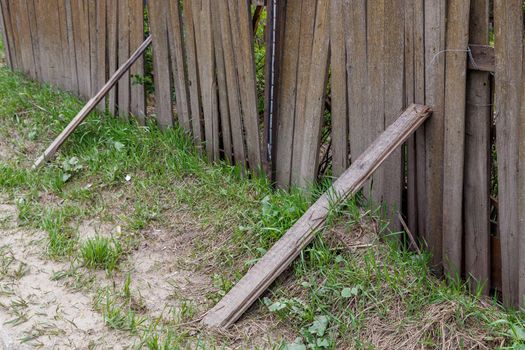 old dusty rickety wooden fence with plank props and grass close up with selective focus.