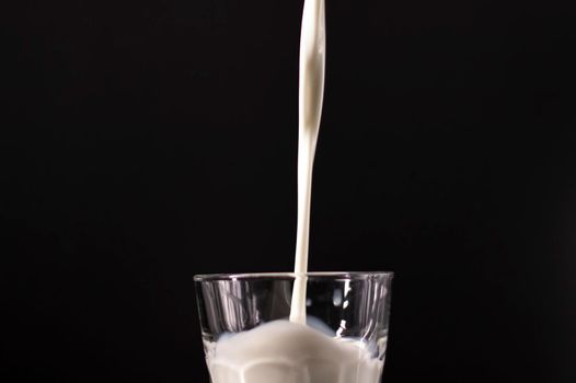 pouring milk in a glass. splash of white liquid isolated on dark background.