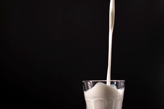 pouring milk in a glass. splash of white liquid isolated on dark background.