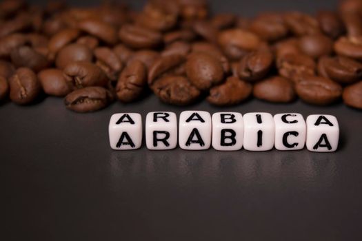 close up of Freshly roasted coffee beans near word ARABICA written with little white cubes. view from top