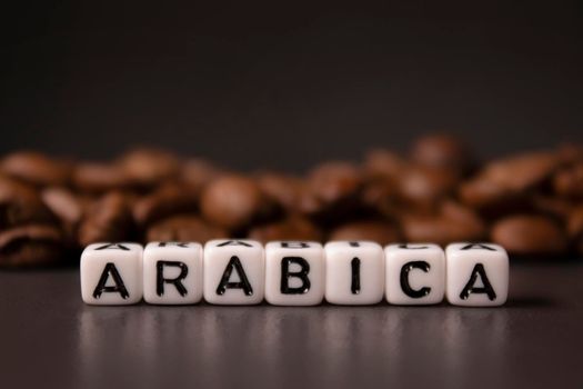 close up of Freshly roasted coffee beans near word ARABICA written with little white cubes. view from top