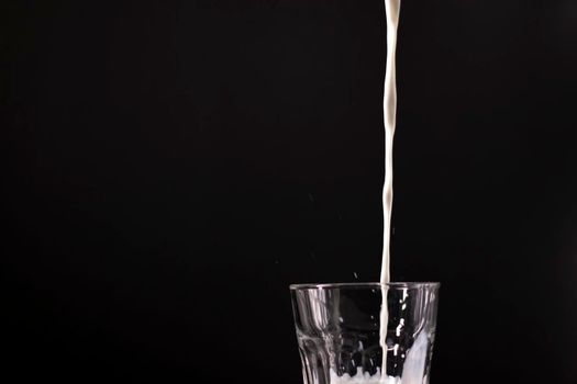 pouring milk in a glass. splash of white liquid isolated on dark background.