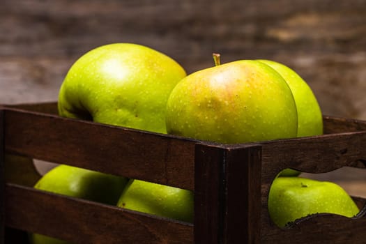 Wooden crate with ripe green apples on wooden table.