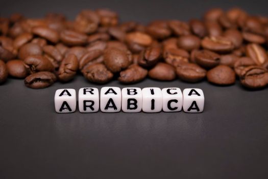 close up of Freshly roasted coffee beans near word ARABICA written with little white cubes. view from top