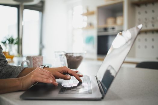 Cropped shot of an unrecognizable woman typing on her laptop during the day at home.