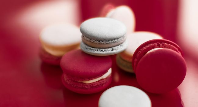 Pastry, bakery and branding concept - French macaroons on wine red background, parisian chic cafe dessert, sweet food and cake macaron for luxury confectionery brand, holiday backdrop design