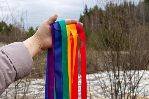 The concept of Valentine's Day, freedom, love. A hand holding rainbow ribbons on the background of a spring river.
