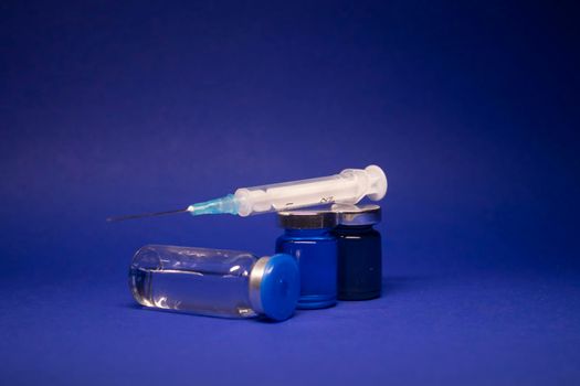 three transparent Vaccine bottle phial with no label, medical syringe injection needle. isolated on blue background. Development of coronavirus vaccine COVID-19. World race in researching. copy space