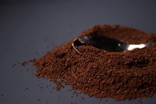 gold teaspoon in a pile of ground or instant coffee on dark background.