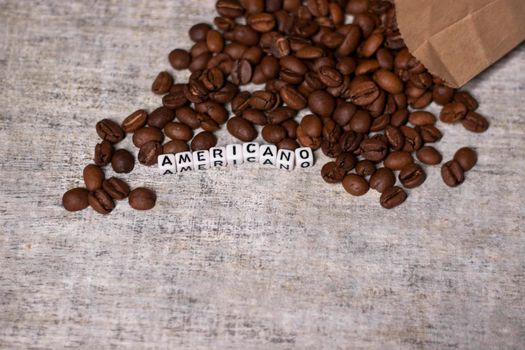 close up of Freshly roasted coffee beans near word AMERICANO written with little white cubes. top view.