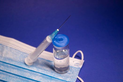 Vaccine bottle phial with no label on blue medical mask and medical syringe with injection needle. isolated on blue background. cure. Development of coronavirus vaccine COVID-19. copy space