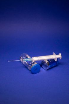 two transparent Vaccine bottle phial with no label, medical syringe injection needle. isolated on blue background. Development of coronavirus vaccine COVID-19. World race in researching. copy space