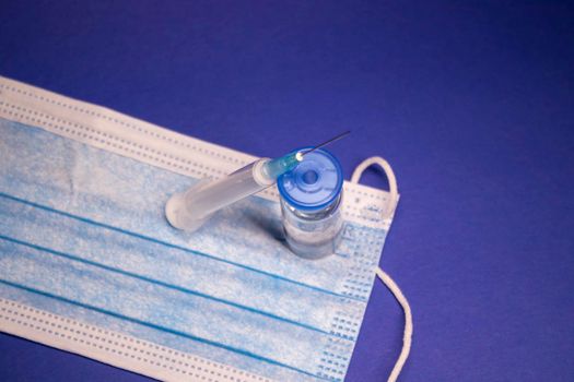 Vaccine bottle phial with no label on blue medical mask and medical syringe with injection needle. isolated on blue background. cure. Development of coronavirus vaccine COVID-19. copy space